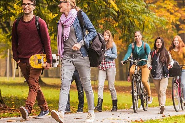 Group of students walk and bike across campus surrounded by colorful fall foliage 